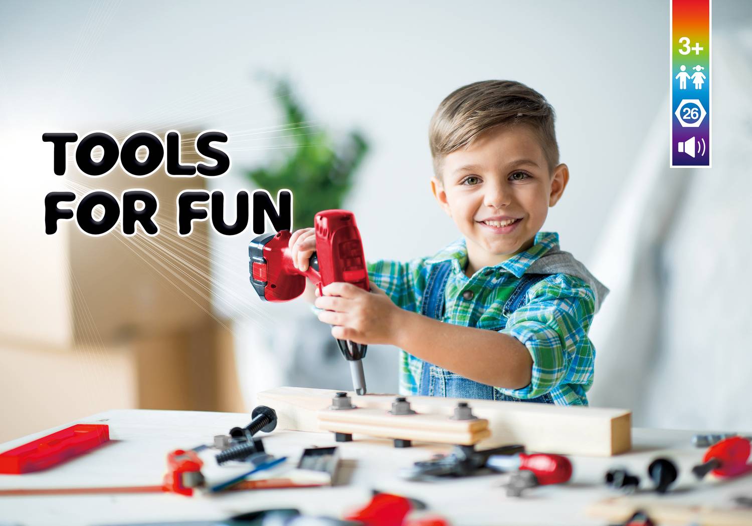 A boy smiles while working with a red toy drill on a piece of wood. Blurred tools can be seen in the background.