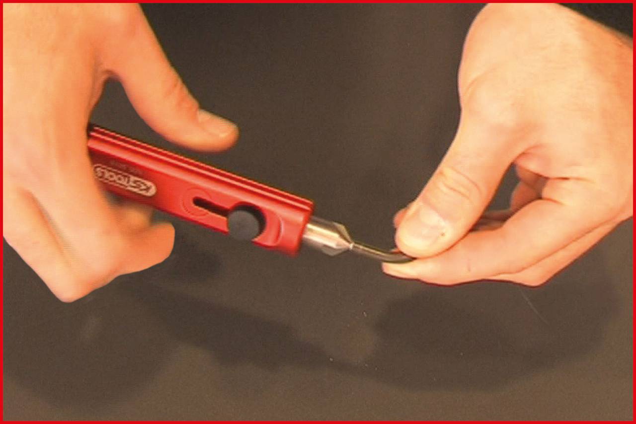 A person is holding a red precision tool with a blade in their hand, ready to carry out precise cutting work.