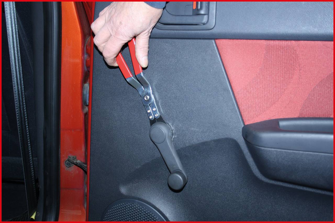 A person is using a specialist tool to remove a manual window winder from a car.