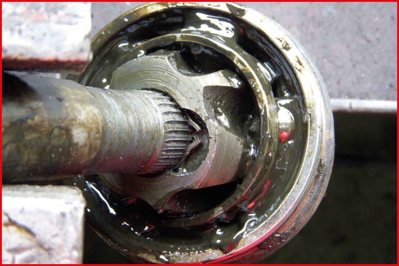 Close-up of a damaged drive joint with broken metal teeth, surrounded by grease. The joint is rusty and worn.