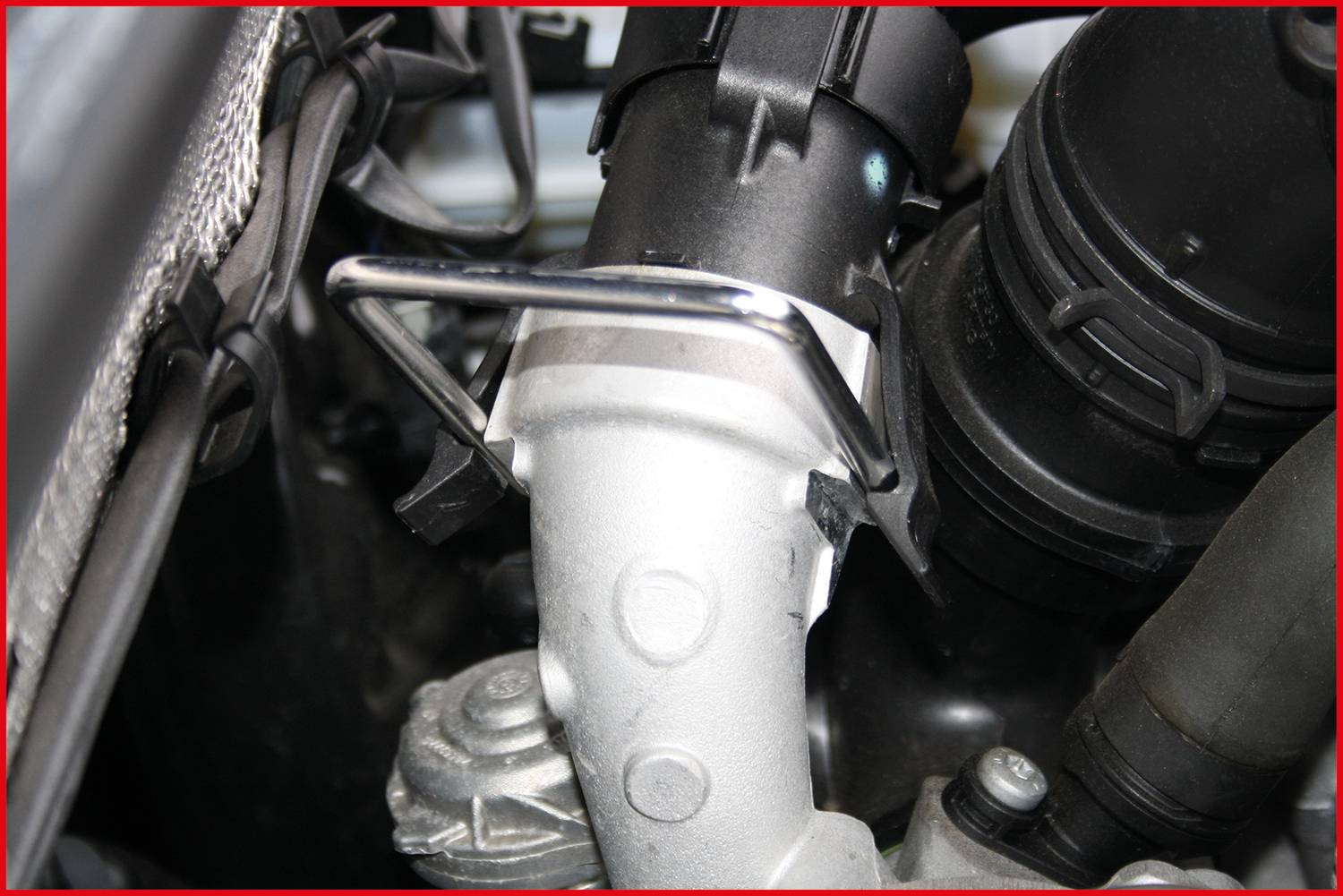 Engine compartment with a close-up view of a component made of metal and plastic, potentially part of the cooling system or exhaust management.