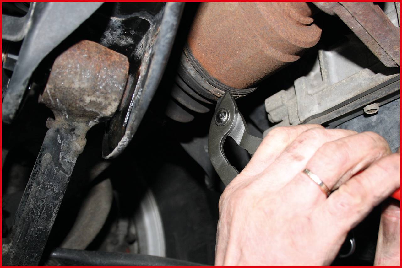 'A person is holding a tool under a vehicle and working on a component near the exhaust pipe.'