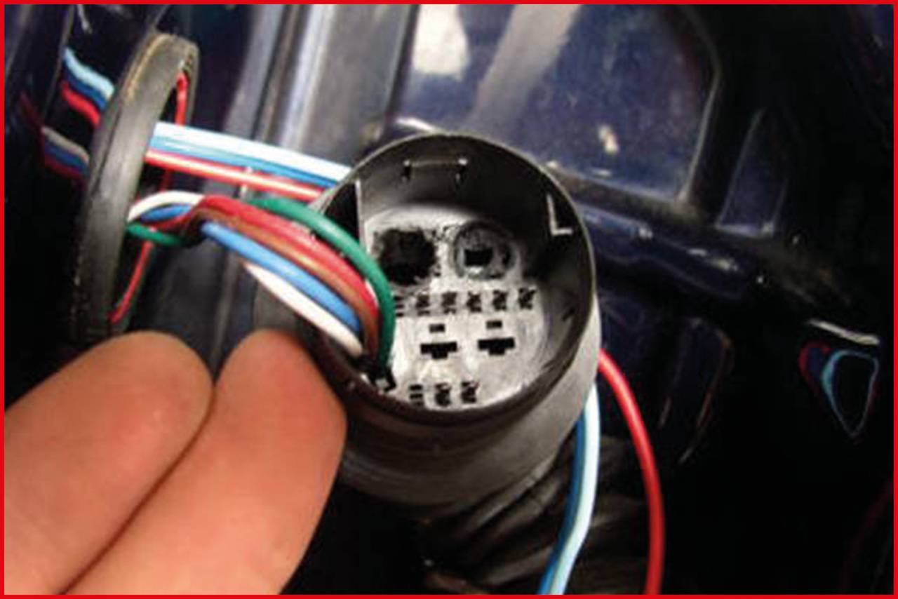 A hand is holding an electrical plug with multiple coloured wires inserted into a round plastic socket.