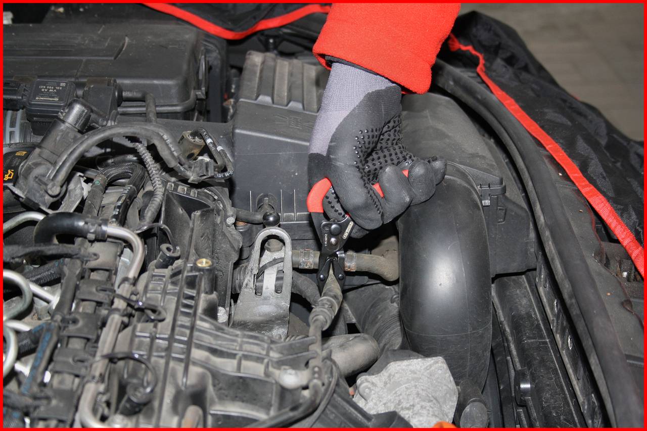 A person wearing red gloves is working in the engine bay of a car, checking or repairing components. The focus is on technical work.