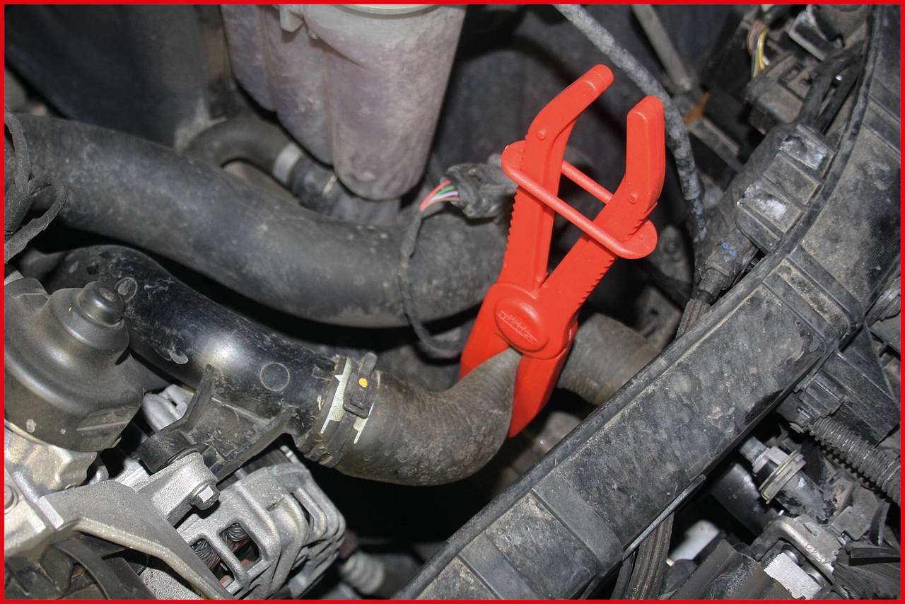 In the image, a car radiator hose is secured with a red clamp to prevent coolant leakage.