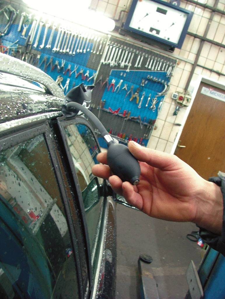 A person is using an air wedge tool to open a car door, likely in a car repair workshop.