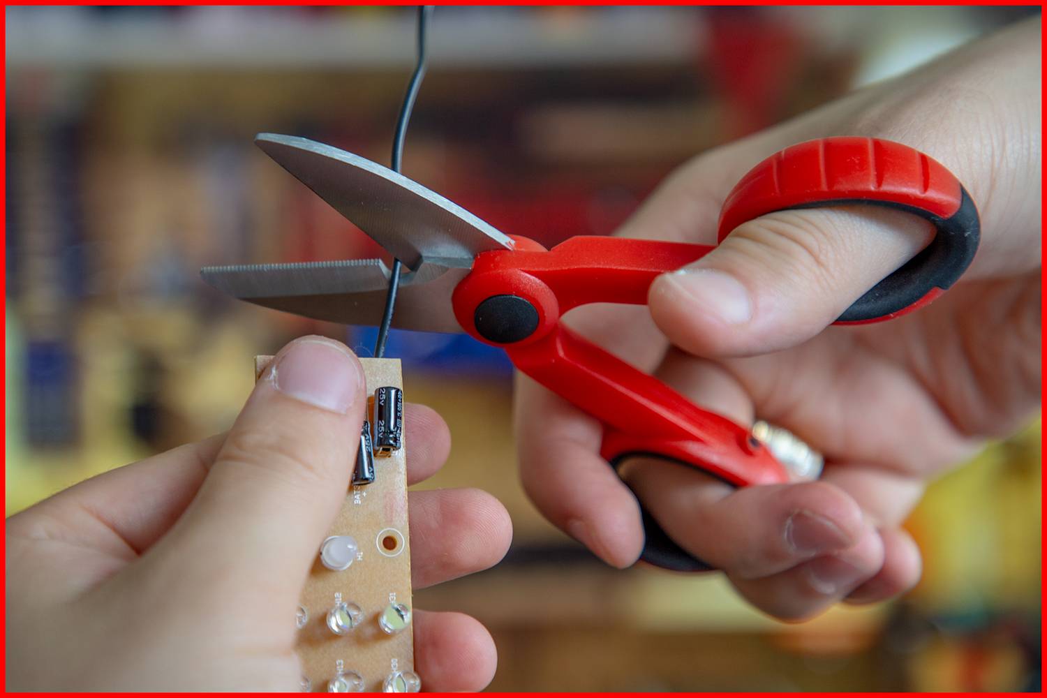 'Close-up of scissors cutting a black cable from a circuit board, illustrating the electronic repair process.'