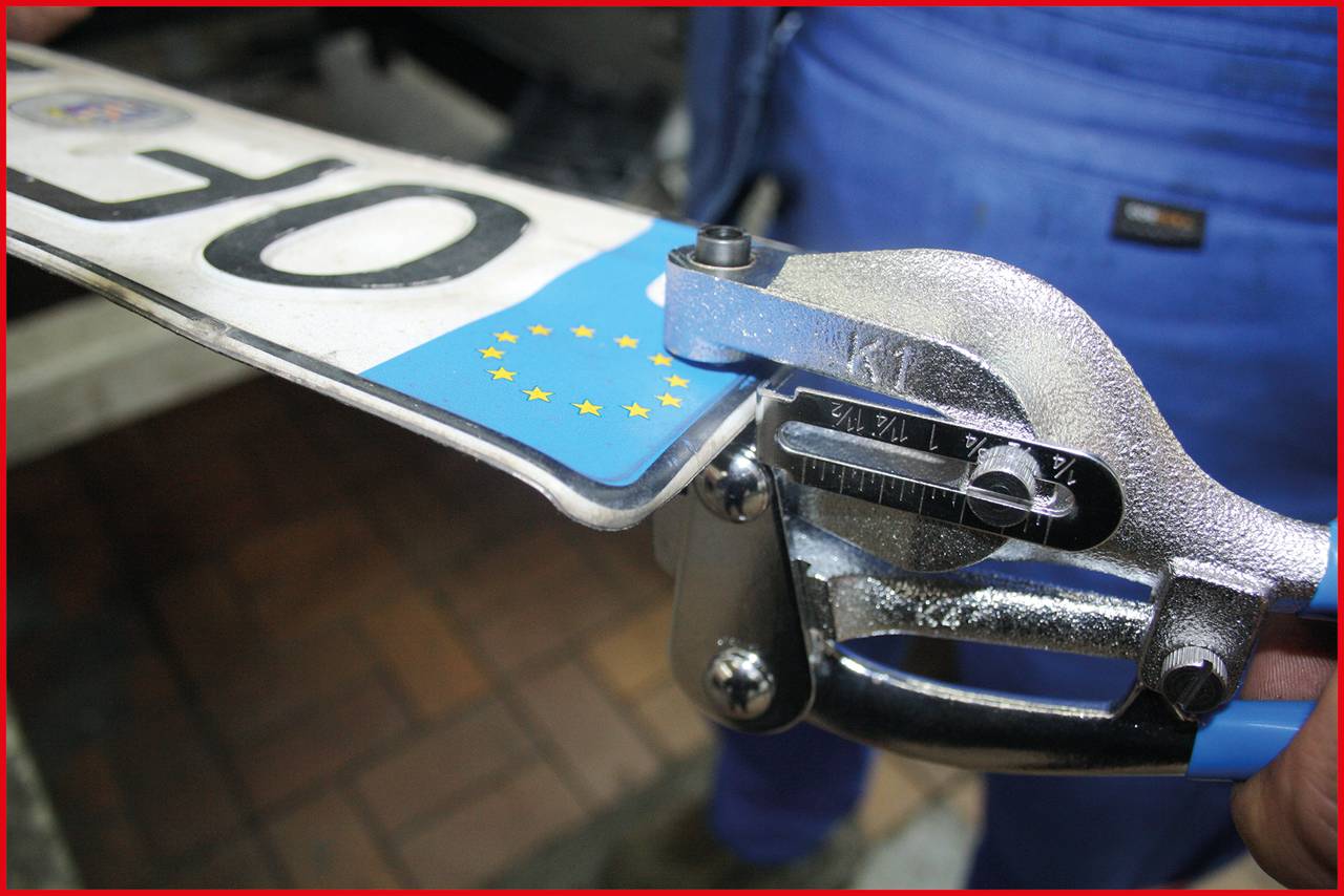 A person is working on an EU licence plate made of metal. The tool is bending or modifying the edge of the plate.