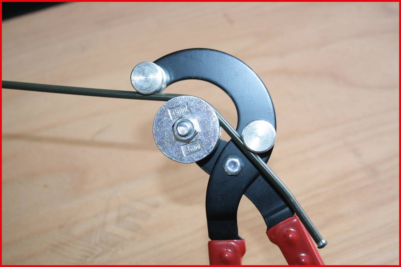 A close-up of a pair of pliers bending a wire at an angled position. The handles of the pliers are red.