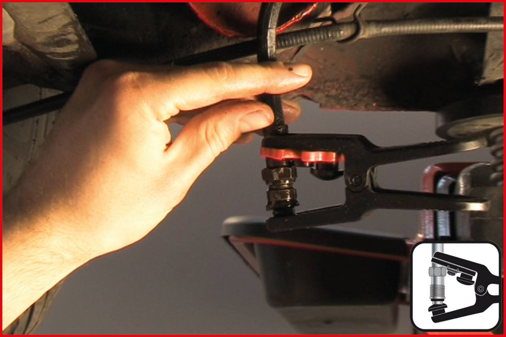 'A hand is using a tool to loosen a car part. Pliers are being used on a red-black component in a workshop environment.'