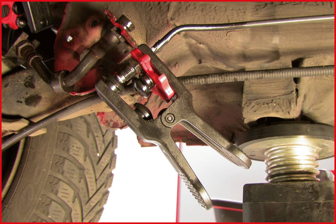 A car jack is lifting a vehicle to carry out repairs on the red brake calliper and brake lines underneath the car.