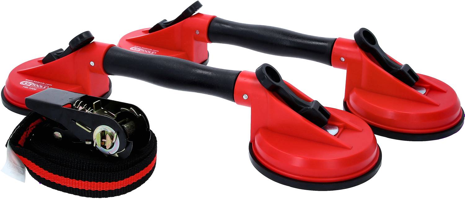 Two red suction lifters with black handles are lying next to a black tension strap with a ratchet. They are suitable for lifting glass.