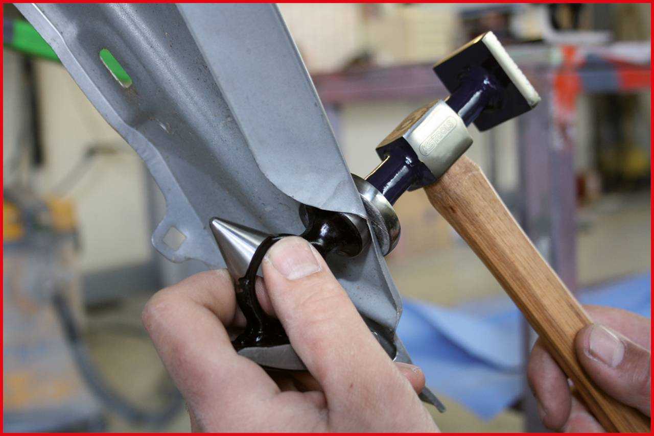 'Close-up of hands working metal with a hammer and a forming tool to bend it into the desired shape.'