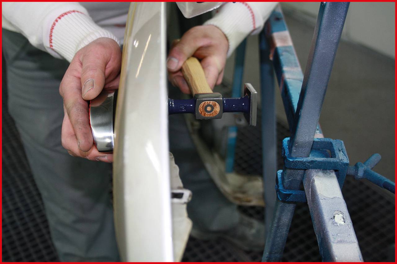 'A person is manually working on a car part, likely metalworking or paint repair, using a specialised tool.'