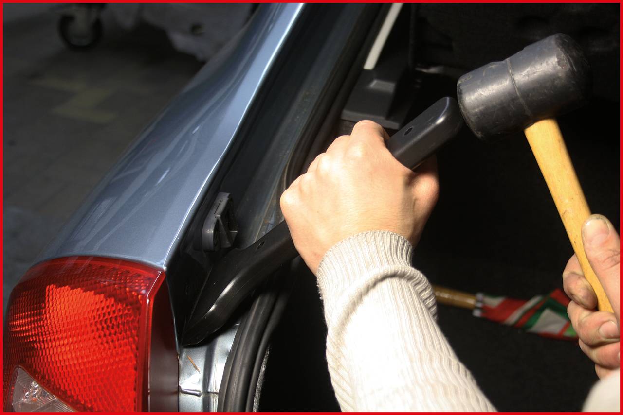 A person is using a rubber mallet and a tool to repair or fit something in a car boot.
