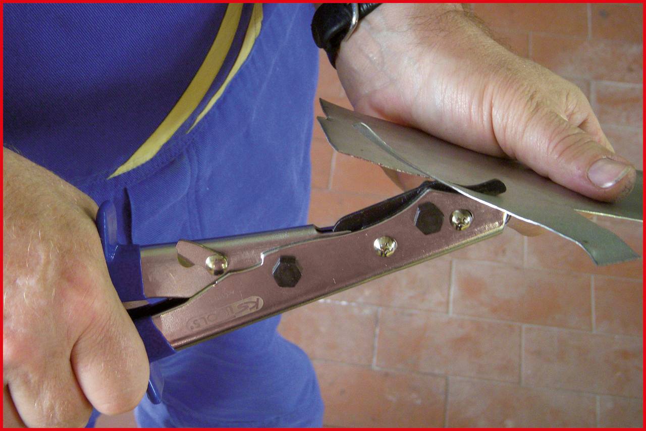 A person is cutting a piece of metal with metal shears. Close-up of hands operating the tool. Tiled floor visible.