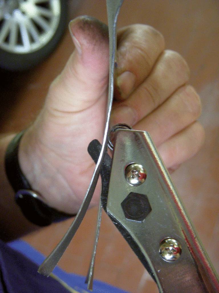 A hand cuts a piece of metal tape with a tool. The background is blurred.