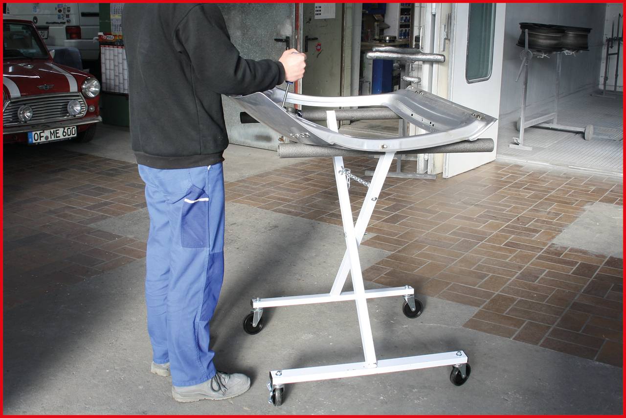 A person wearing blue trousers is standing next to a mobile metal frame with a curved surface in a workshop.