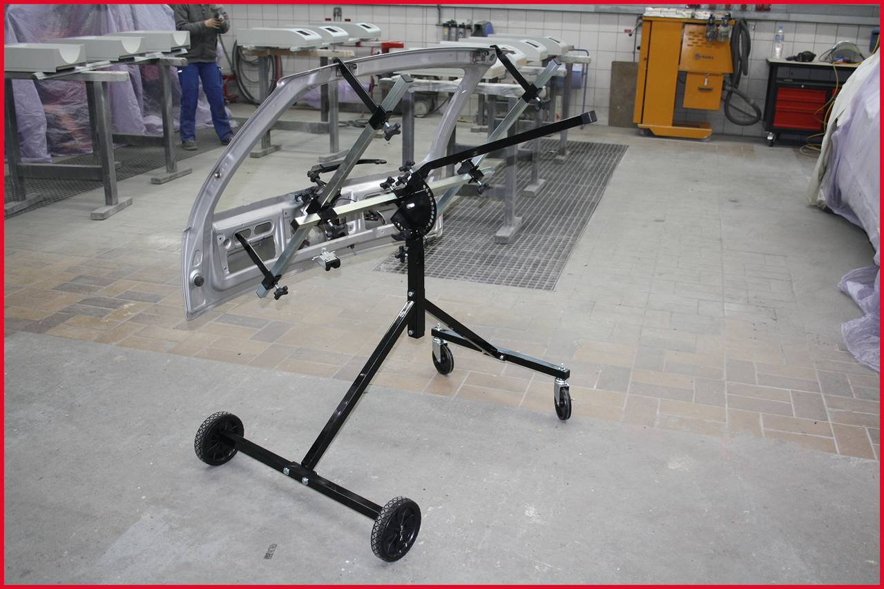 A workshop trolley with wheels stands in a car workshop, surrounded by tools and vehicle parts. It is used for holding large components.