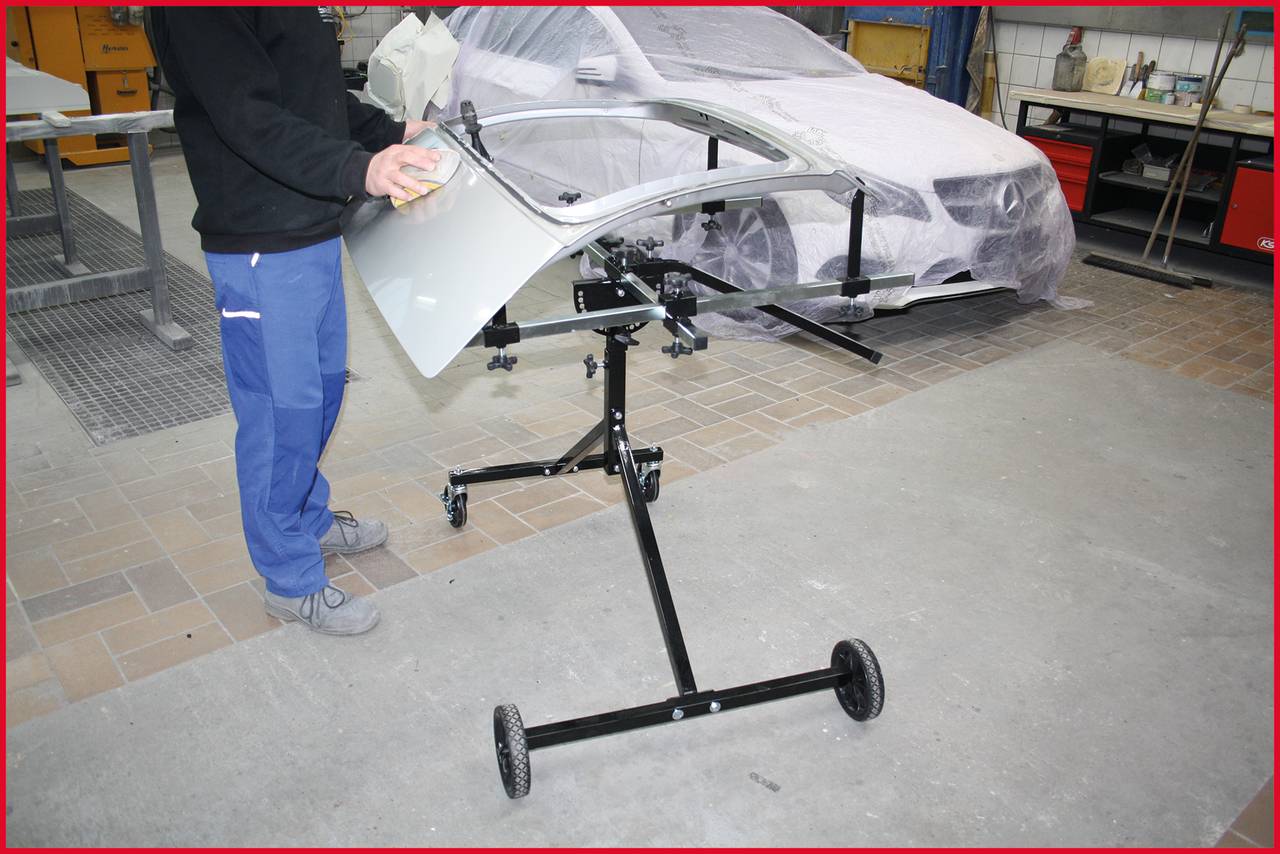 A person is grinding a car door on a stand in a workshop. In the background, a car is partially covered.