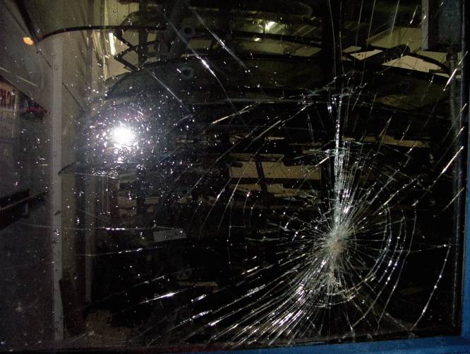 A large window pane with a spider's web-like fracture pattern in the centre, surrounded by light reflections.