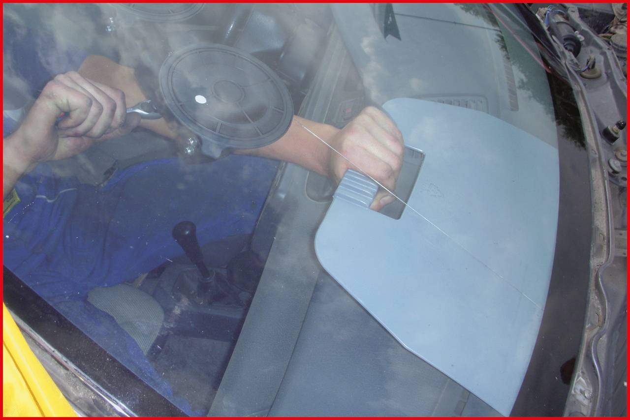 A person is repairing a windscreen with a specialised tool. Their hand is close to the glass, working to fix a crack.