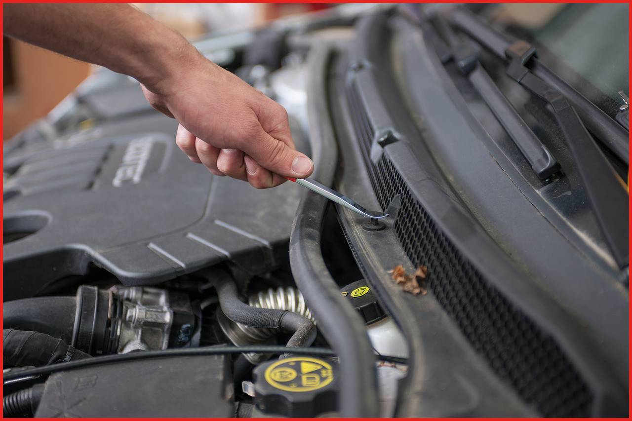 A person is repairing the engine compartment of a car with a screwdriver, close-up of hand and engine bay details.