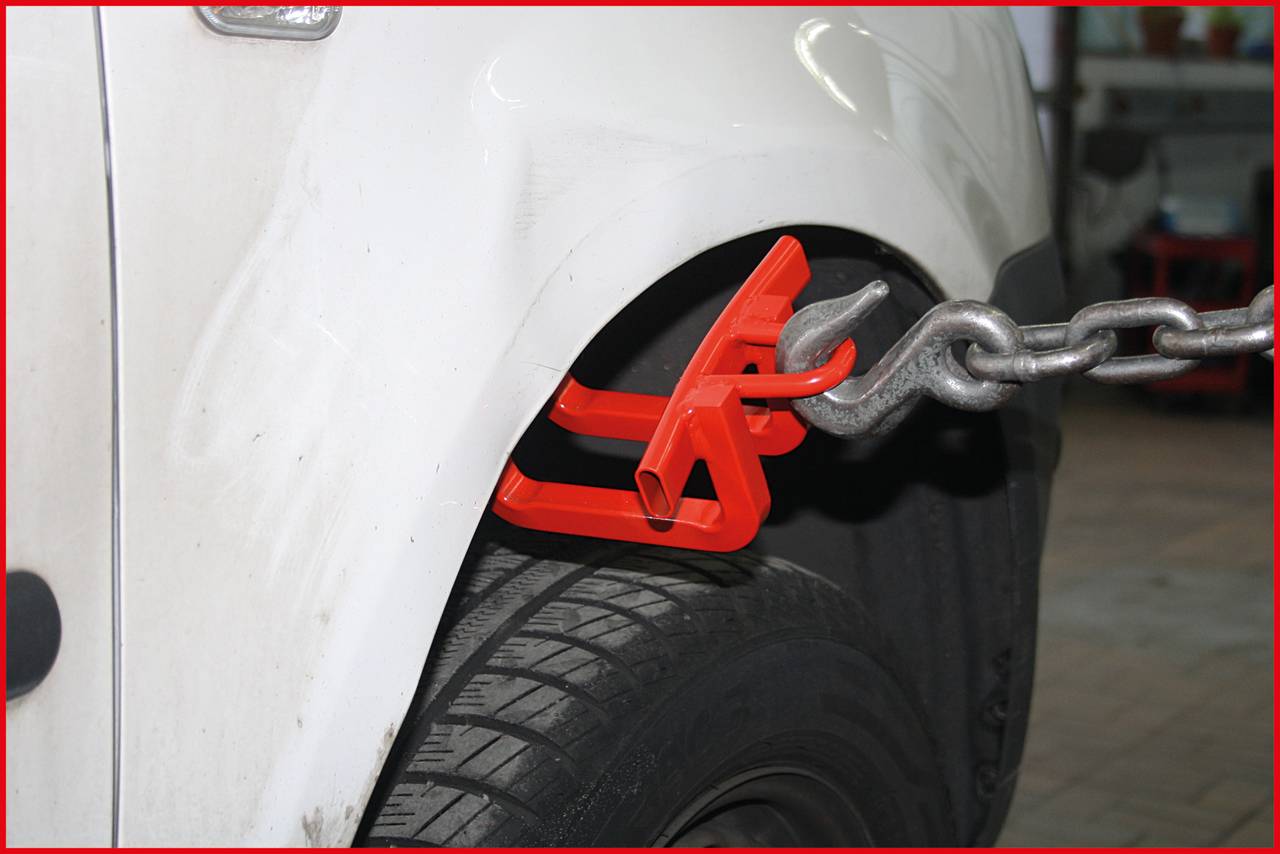 A white car is secured with a red clamp on the front bodywork and a chain, potentially in a garage or workshop.