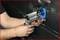 A person is repairing a car door with a specialist tool positioned on the bodywork to remove a dent.