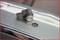 A parking sensor is resting on a car bumper next to a round hole in which it is to be installed.