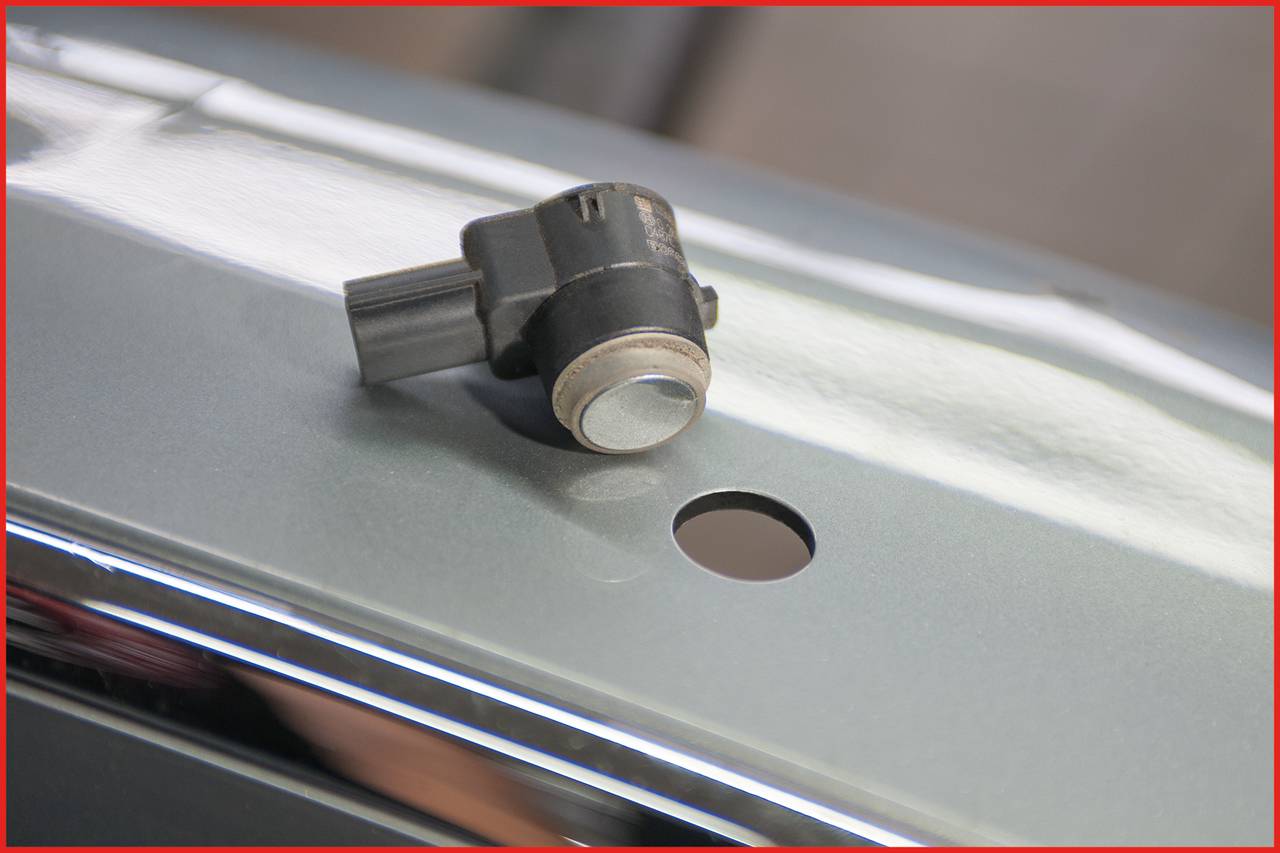 A parking sensor is resting on a smooth, glossy surface. Next to it is a small round hole, suitably sized for the sensor.