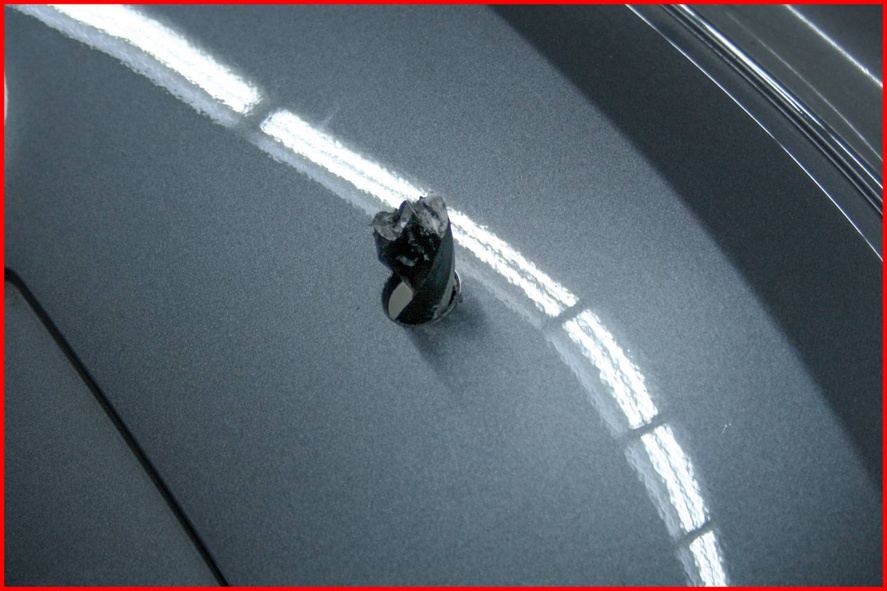 Surface of a car with a dent and paint damage caused by a heavy object, illuminated by reflective white stripes.