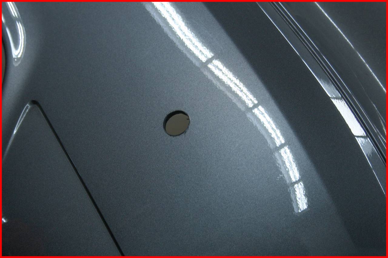 Close-up of a grey, shiny metal component with a small round hole in the centre. Reflected light is visible.