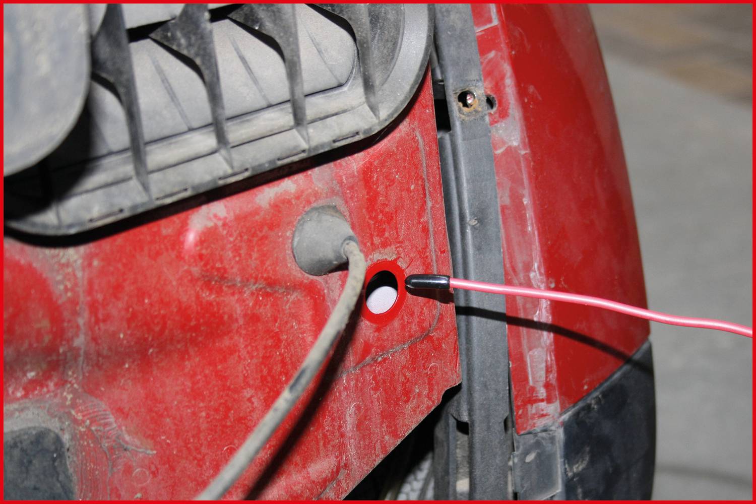 A cable is being pulled through a hole inside a red vehicle. The area looks dusty and somewhat dirty.