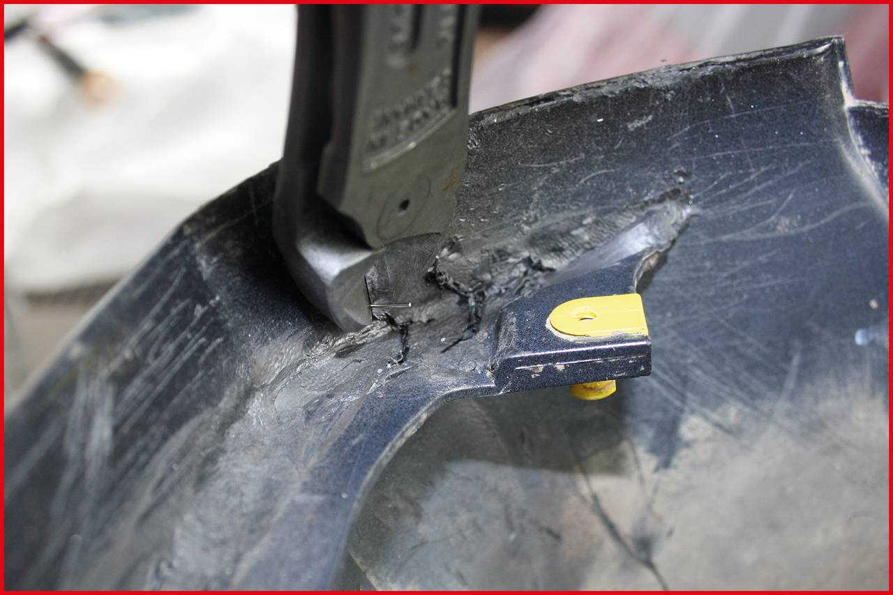 A black plastic part is being worked on with a knife. The sharp blade cuts through the material, yellow detail visible.