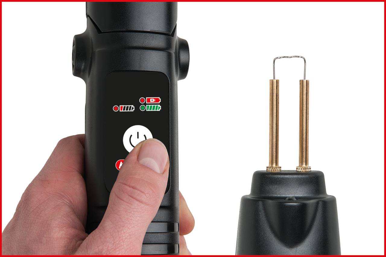 A person is holding an electronic device with buttons and lights. Next to it is a black charging base with two metallic contacts visible.