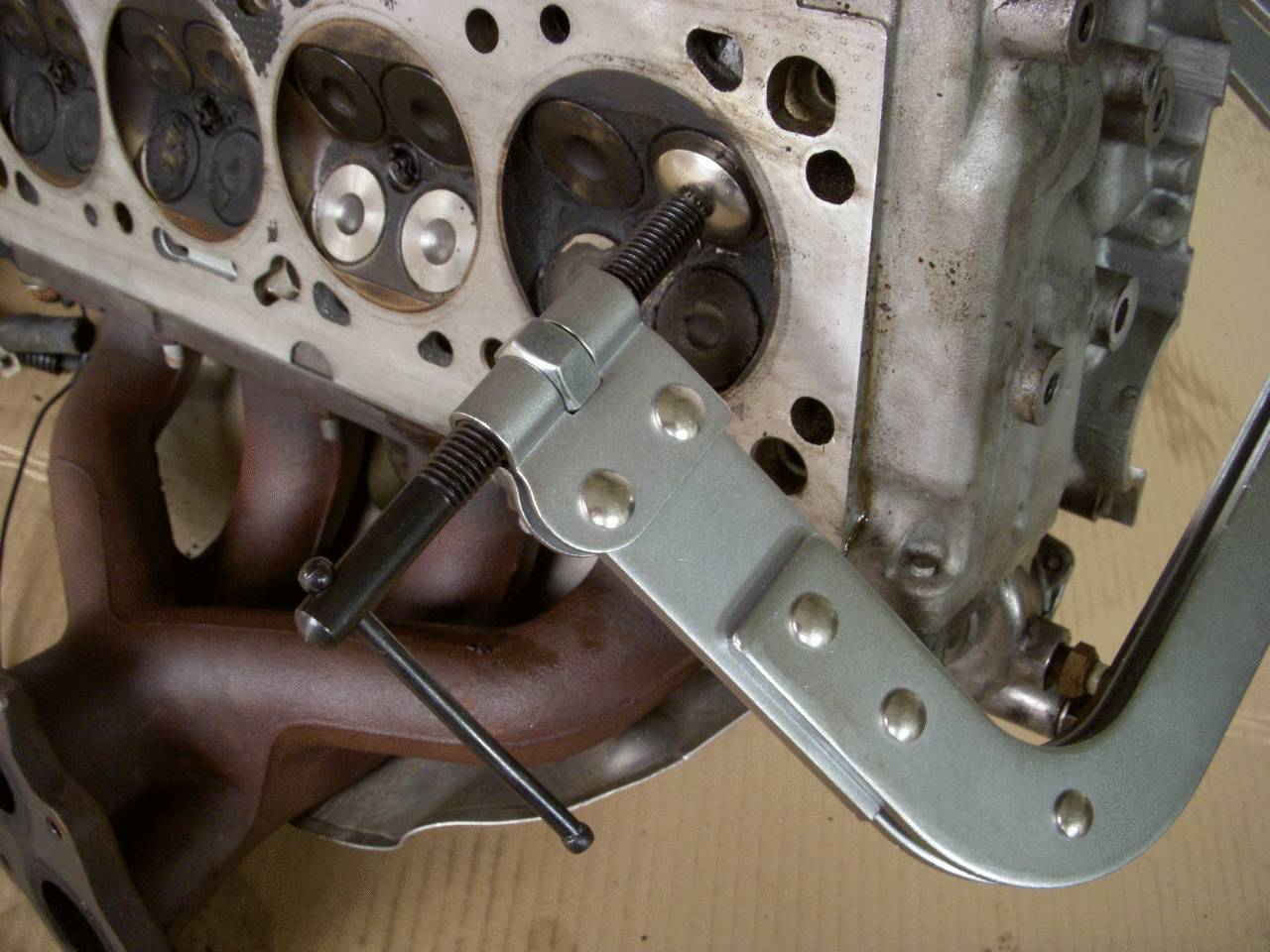Metal clamp holds the car cylinder head gasket in place. The engine block shows valves and a manifold. Mechanical maintenance.