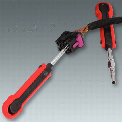 A red, long screwdriver reaches into a black plastic connector with cables. Tool for electrical maintenance.