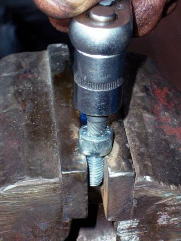 Close-up of a metal pliers gripping a screw, while a hand with a ratchet tool tightens the nut.