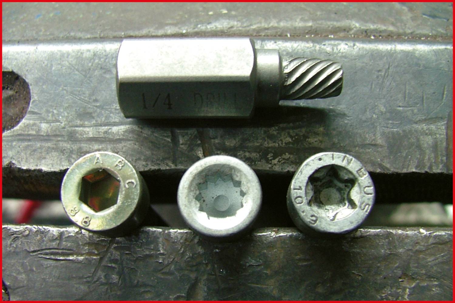 'Three screw heads and a metal drill bit are lying on a vice. The screws show different internal hexagon designs.'