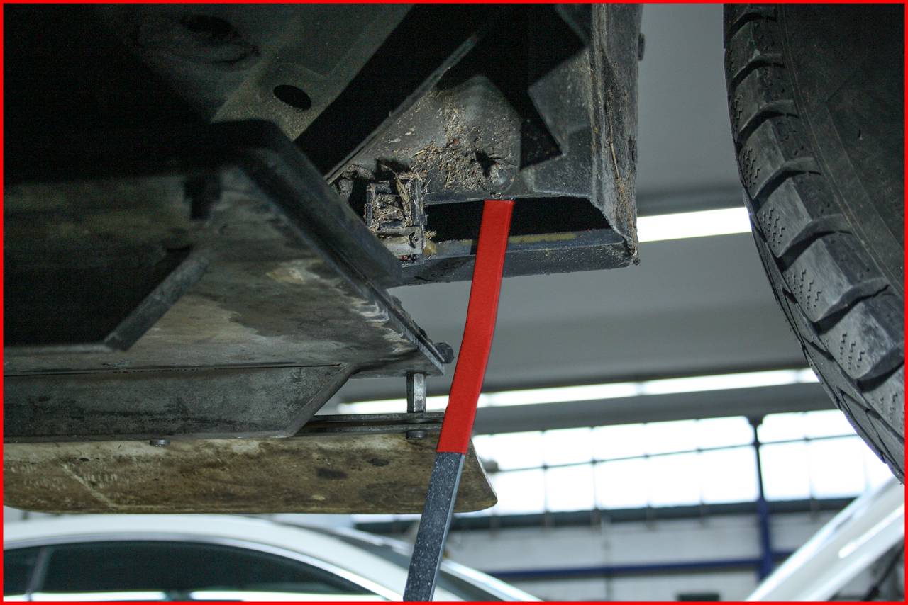 The image shows the underside of a car with a damaged chassis, visible through detached parts and exposed components.