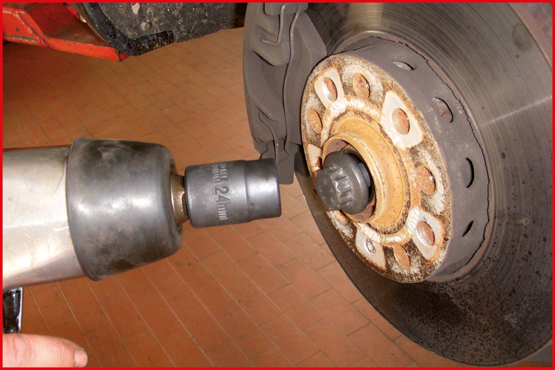 A person is tightening a wheel nut with an impact driver on a car tyre. The tyre is mounted on a brake disc.