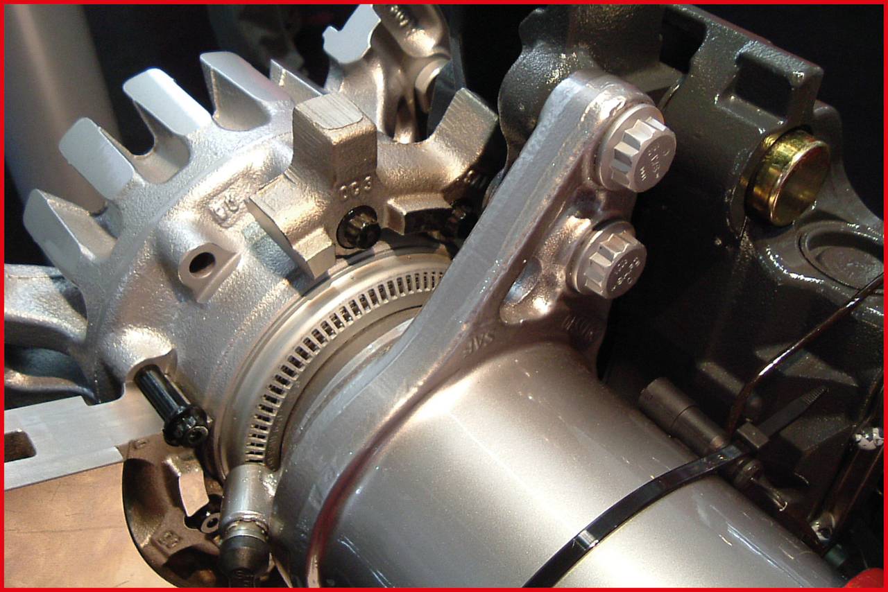 Detailed view of a metal machine component with teeth and bolts, likely a part of an engine or turbine mechanism.