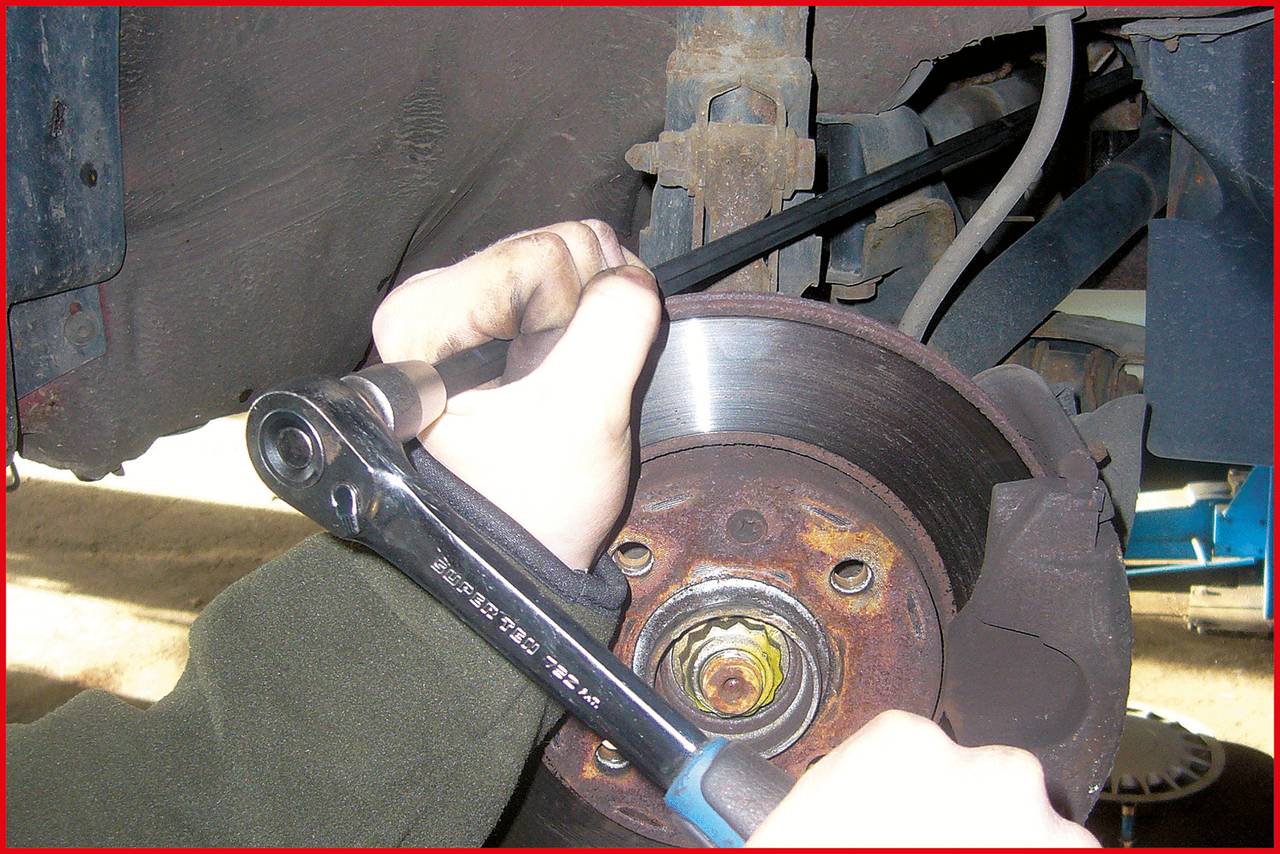 Person repairing car brakes with a ratchet. Close-up of the brake system. Brake disc, brake pad, and dust are visible.