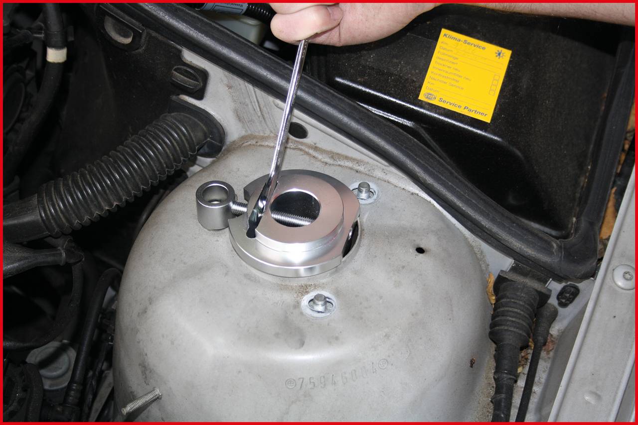 A mechanic uses a tool to tighten a screw on a car part in the engine bay.