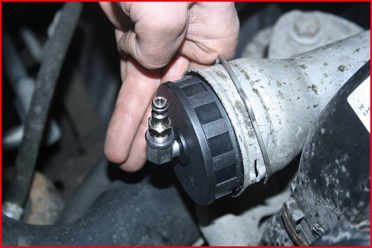 'A hand is securing a round, black plastic cover onto a metal pipe with a screw connection in the foreground.'