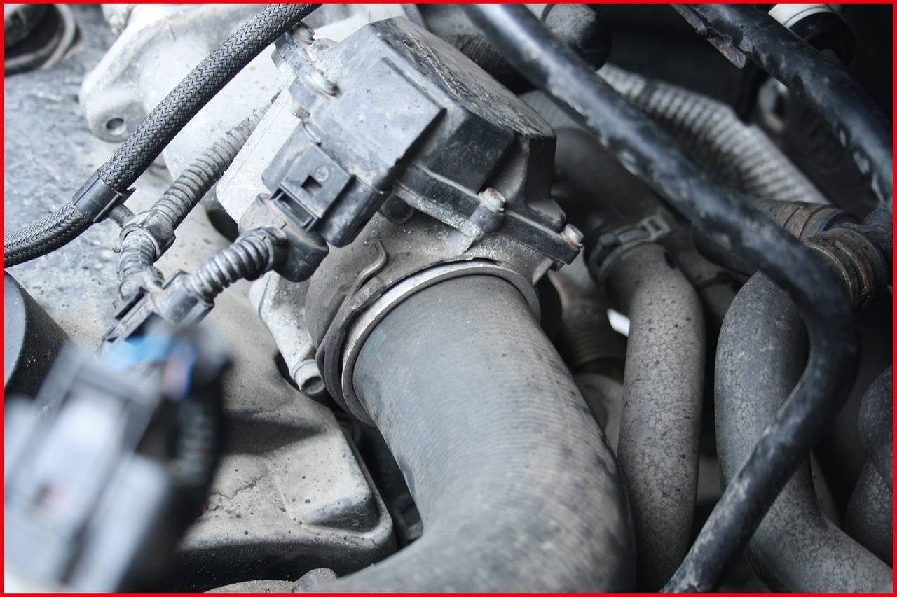 Engine bay of a vehicle focusing on a grey hose and various cables and connections.