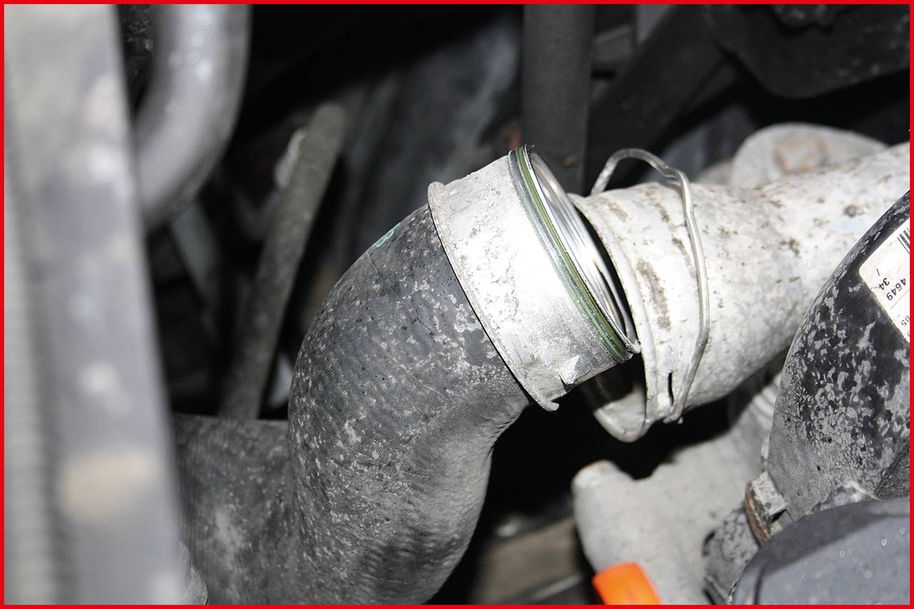 Close-up of a damaged radiator hose in an engine compartment. The hose is loose at a clamp and slightly displaced.