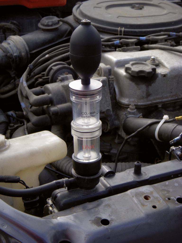 A CO₂ measuring device is attached to a vehicle engine to check the CO₂ content. Part of the engine is visible behind the device.