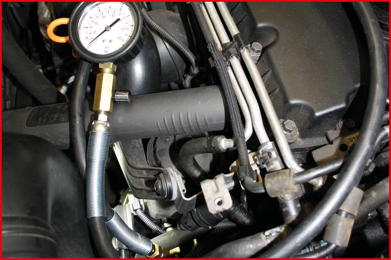 A manometer measures the pressure in an engine component with numerous pipes and wires in the foreground.